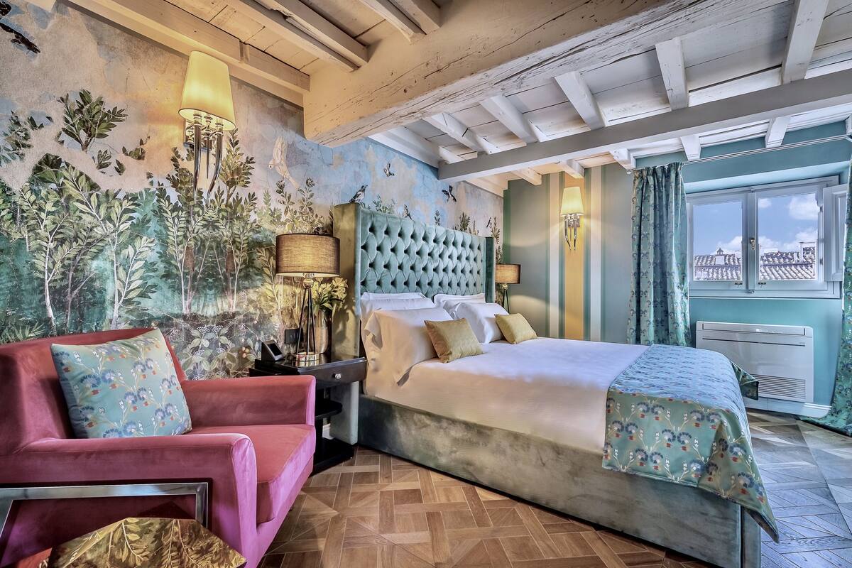 A bedroom with a large bed, a red sofa, a wall mural, and a window with curtains.