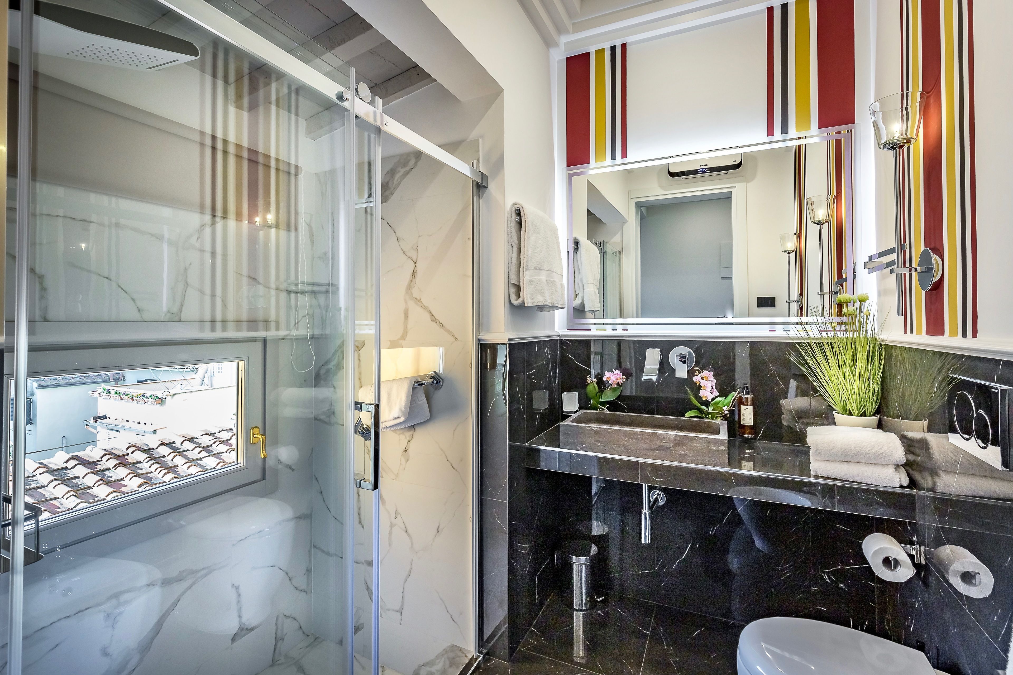 A modern bathroom with a glass-enclosed shower, a black marble sink, and a large mirror with striped wall decorations.