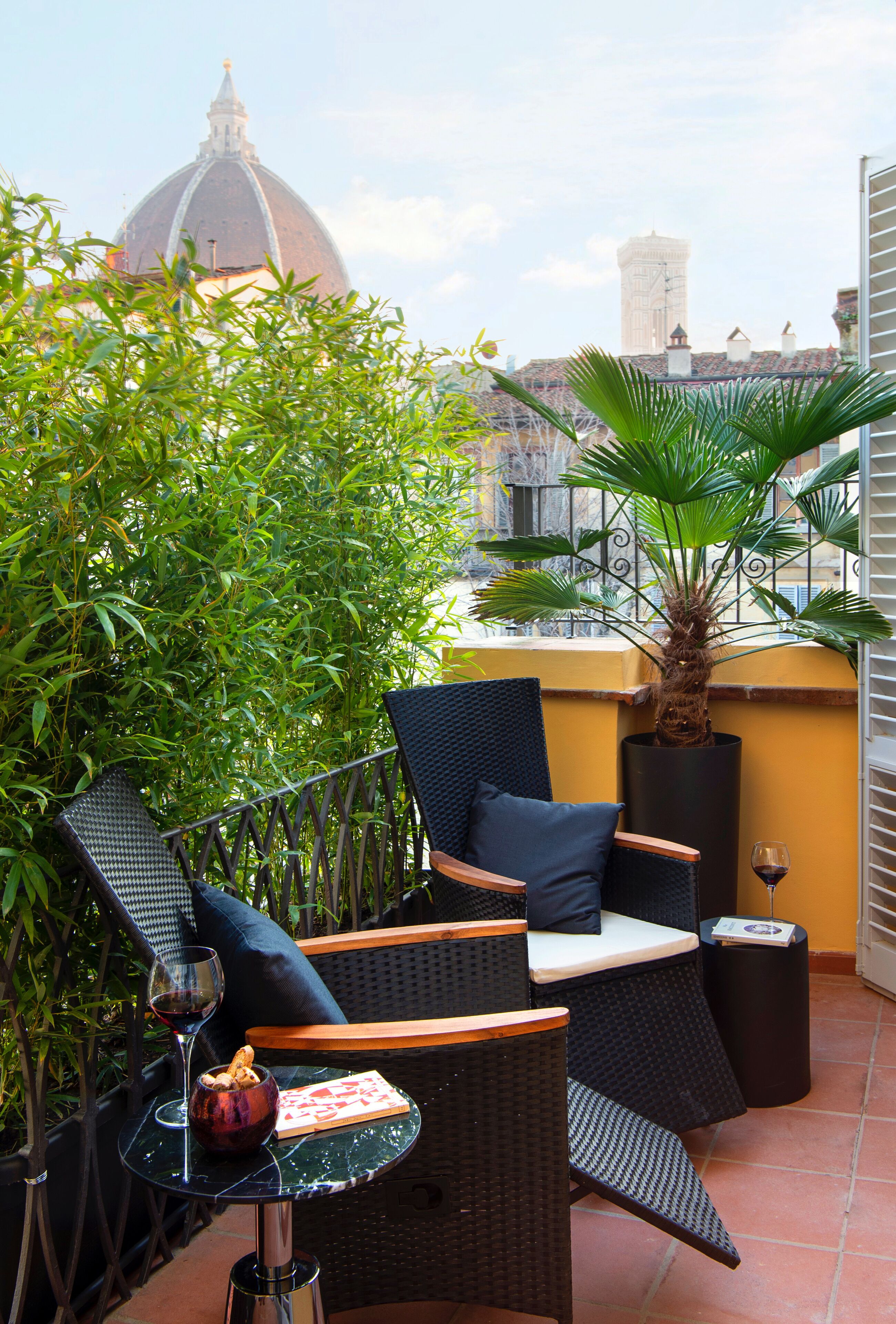 A balcony with wicker furniture, a potted plant, and a wine glass.