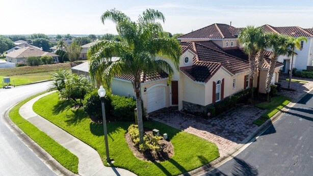 A residential house with a curved driveway, palm trees, and a well-maintained lawn.