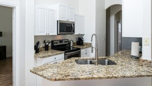 A modern kitchen with white cabinets, a granite countertop, a stainless steel sink, a microwave, and a stove.