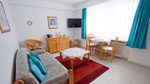 Ein möbliertes Zimmer mit Sofa, kleinem Tisch, Fernseher, Kommode und Essbereich.