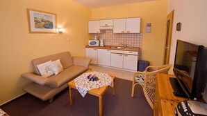 Un espacio habitable compacto con sofá, una mesita, televisión y kitchenette.