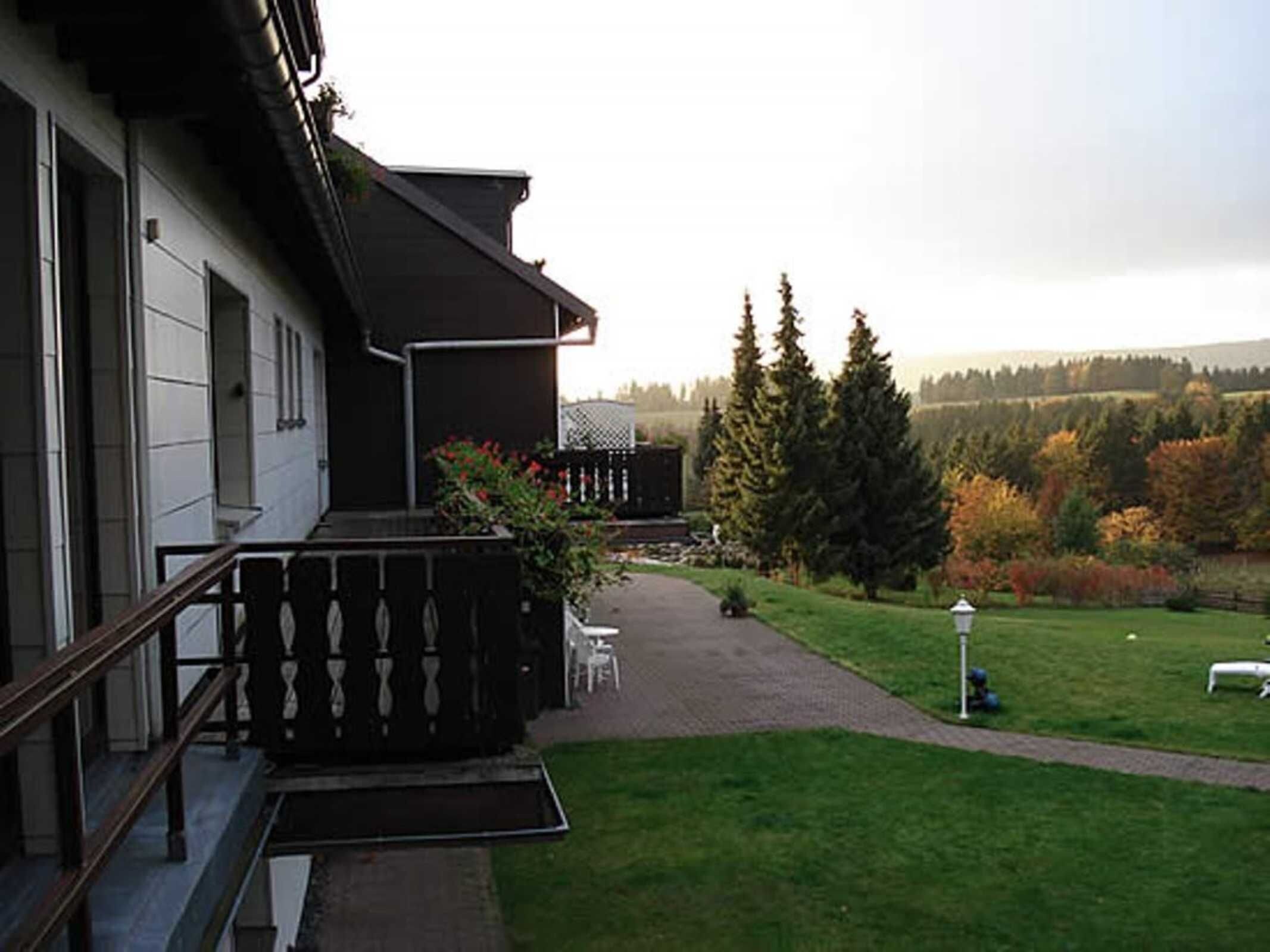 A building with a balcony, a paved pathway, and a grassy area with trees.