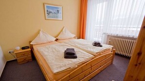 Una cama doble con estructura de madera, una mesita de noche con lámpara y una ventana con cortinas.