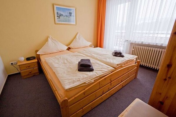 A double bed with a wooden frame, a bedside table with a lamp, and a window with curtains. - Apartment 4 - Panorama of the house (Sankt Andreasberg)
