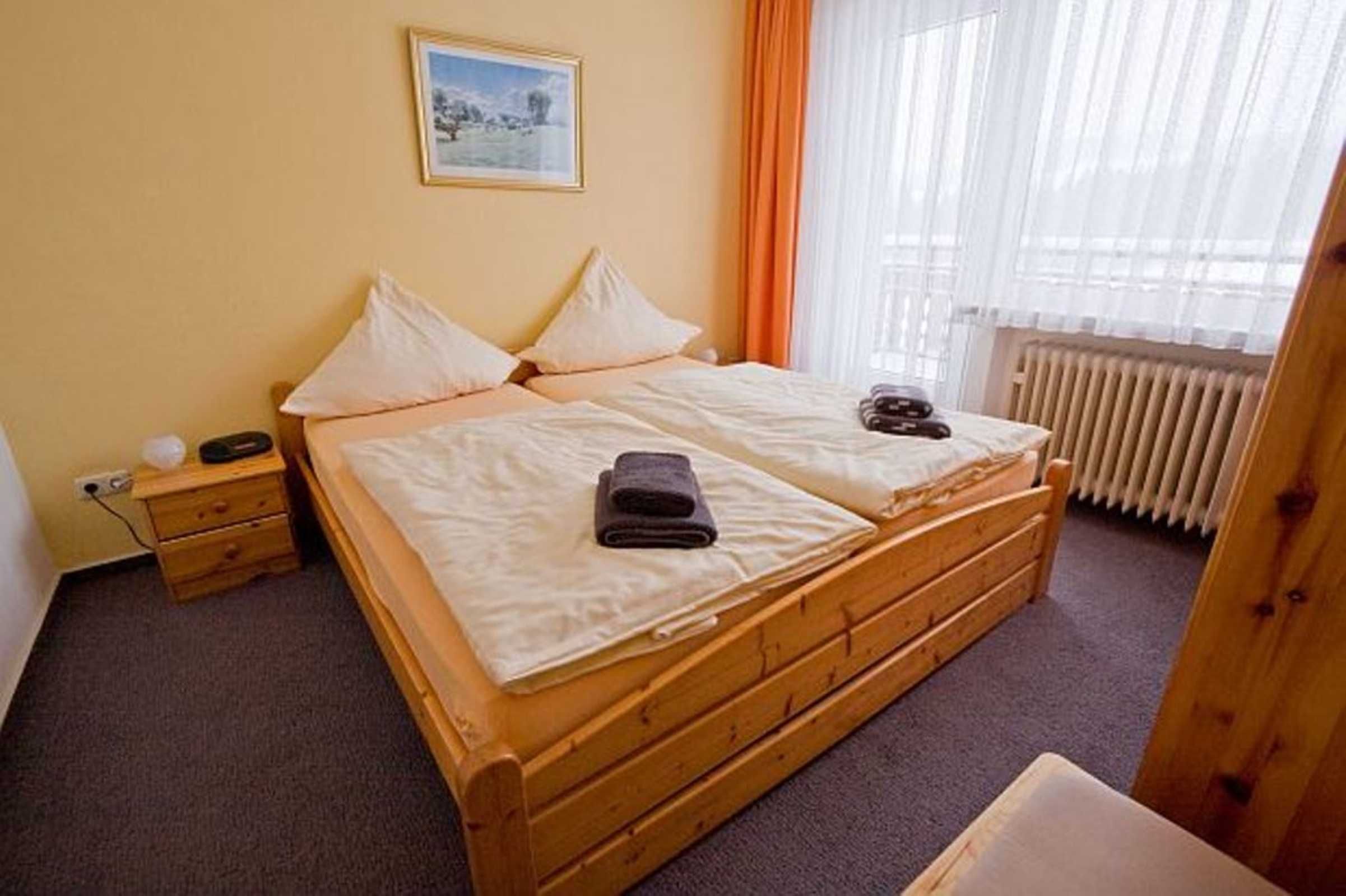 Una cama doble con estructura de madera, una mesita de noche con lámpara y una ventana con cortinas.