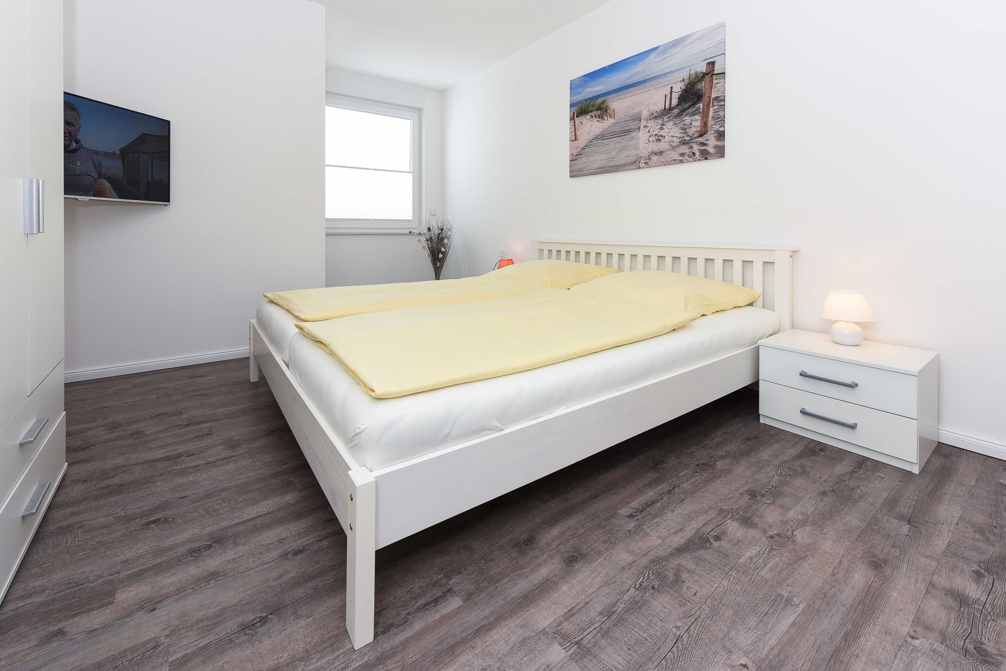 A bedroom with a bed, a nightstand, a lamp, a TV, and a window.