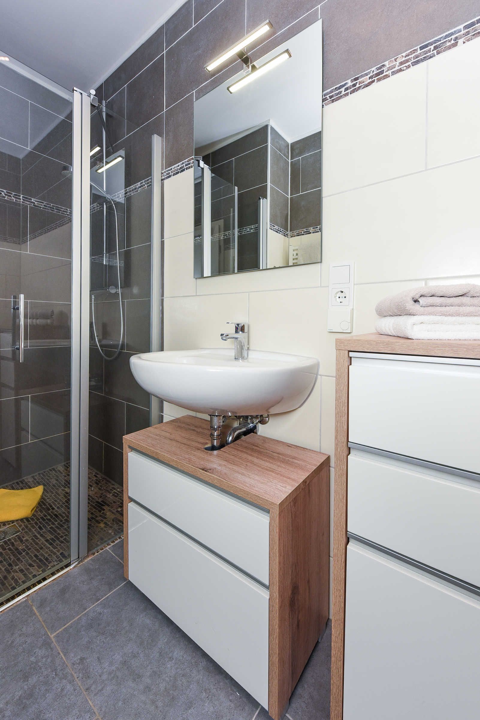 A modern bathroom with a glass-enclosed shower, a white sink, and a wooden vanity.