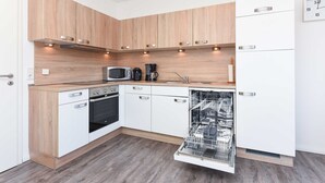 A modern kitchen with wooden cabinets, a dishwasher, a microwave, and a coffee maker. - Apartment Hanseatic city Zwolle (Wittmund)