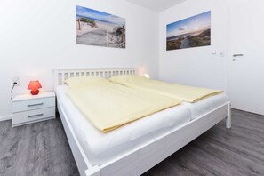Une chambre à coucher avec un lit blanc, une table de chevet avec une lampe et deux tableaux accrochés au mur.