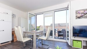 A modern living room with a dining area, a TV, and a sliding glass door leading to an outdoor patio. - Apartment Hanseatic city Zwolle (Wittmund)