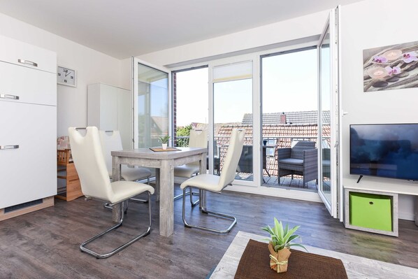Un salon moderne comprenant un coin repas, un téléviseur et une porte-fenêtre coulissante donnant sur une terrasse extérieure.
