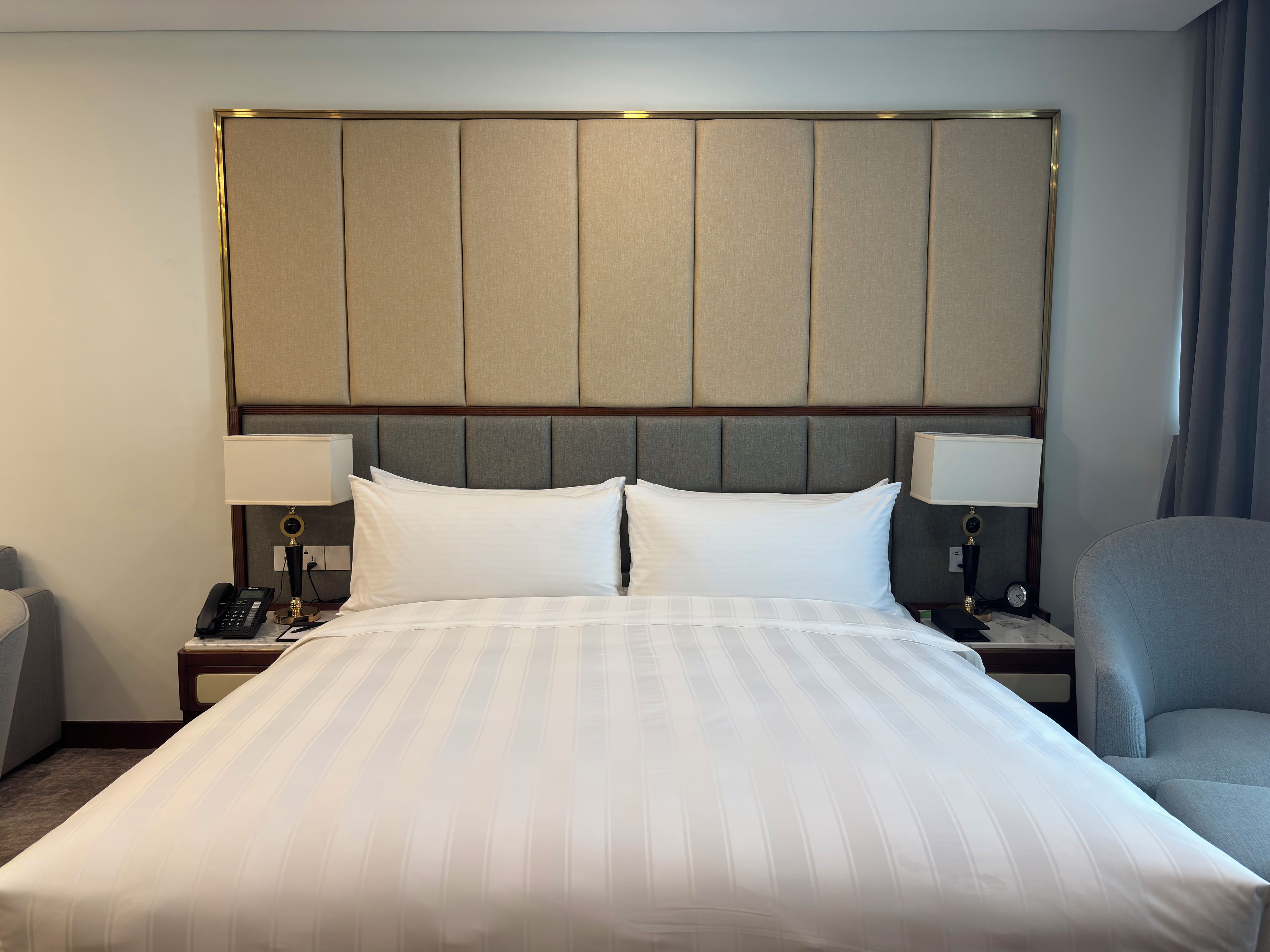 A hotel room with a large bed, two bedside lamps, a telephone, and a chair.