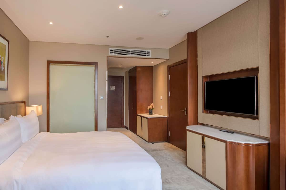 Habitació d'hotel amb un llit gran, un televisor penjat a la paret i un escriptori amb un ram de flors.