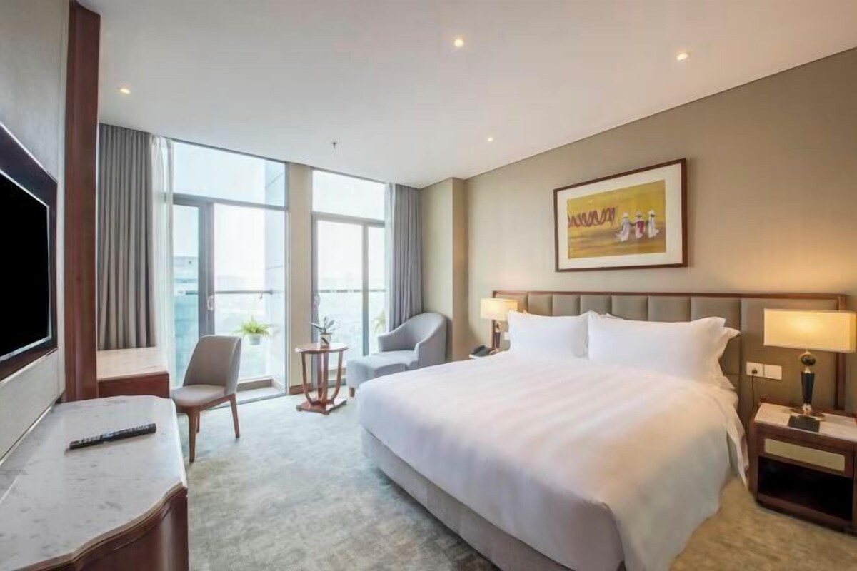 Habitación de hotel con una cama grande, un escritorio, una silla, un televisor y una ventana con cortinas.