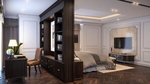 A bedroom with a large dark wood bookcase, a leather armchair, a bed with a grey and white duvet, a flat-screen TV mounted on the wall, and a herringbone wood floor. - Wyndham Garden Hanoi (Hanoi)