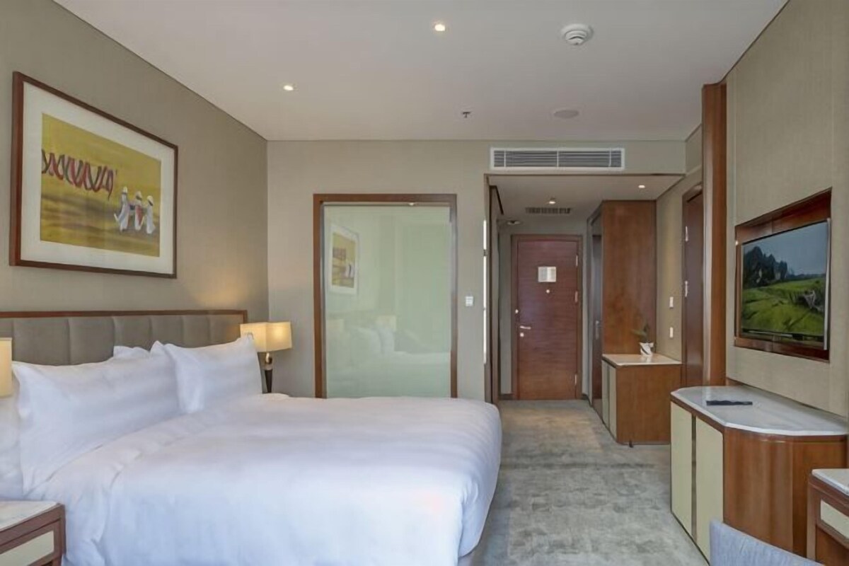 Habitación de hotel con una cama grande, televisión, escritorio y puerta que da a un baño.