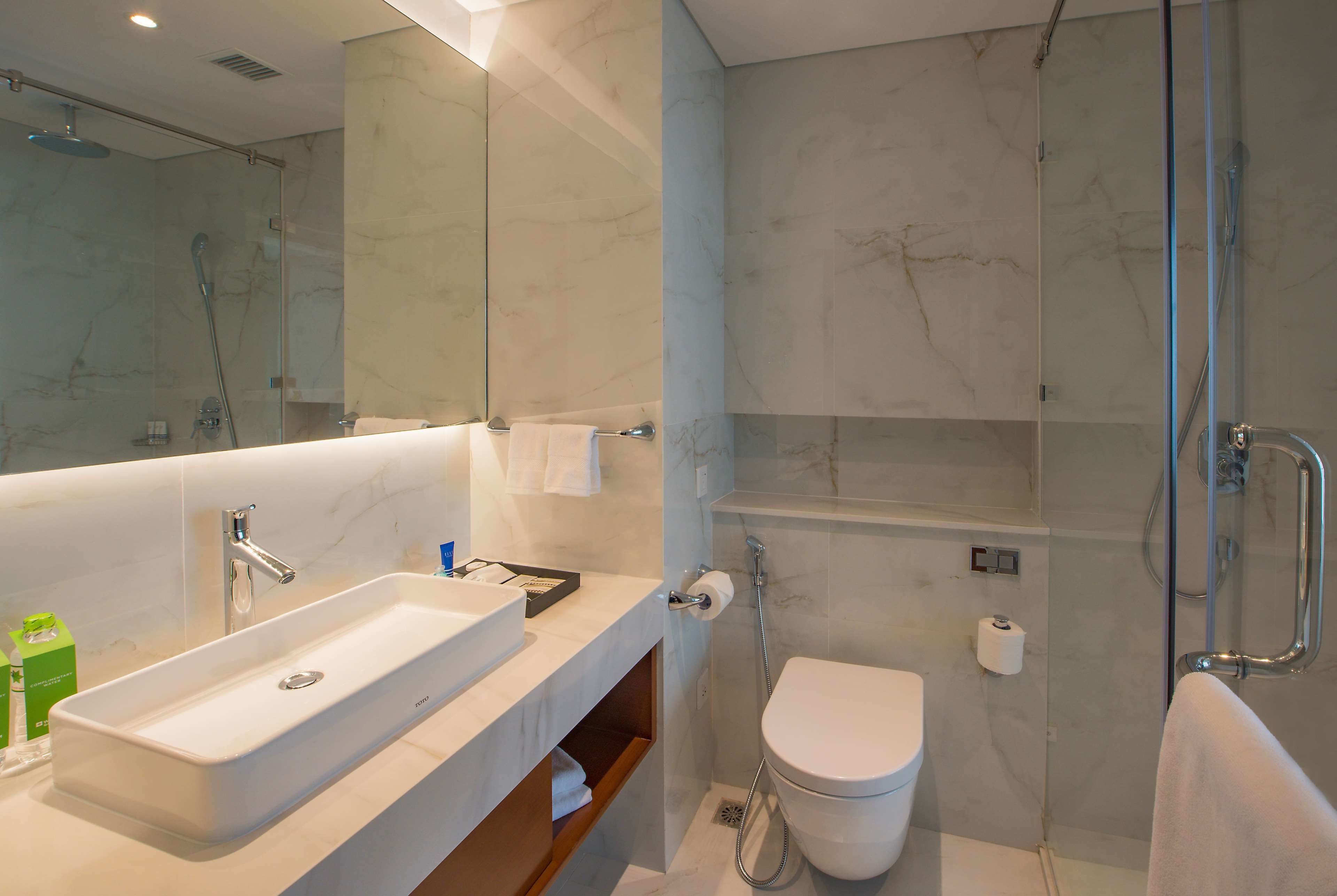 Un baño moderno con un espejo grande, un lavabo, un inodoro y una ducha.