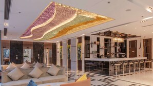 A modern hotel lobby with a large seating area, a bar, and a decorative ceiling light. - Wyndham Garden Hanoi (Hanoi)