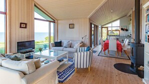 Amplia sala de estar con televisor grande, asientos cómodos, comedor y vistas al exterior.