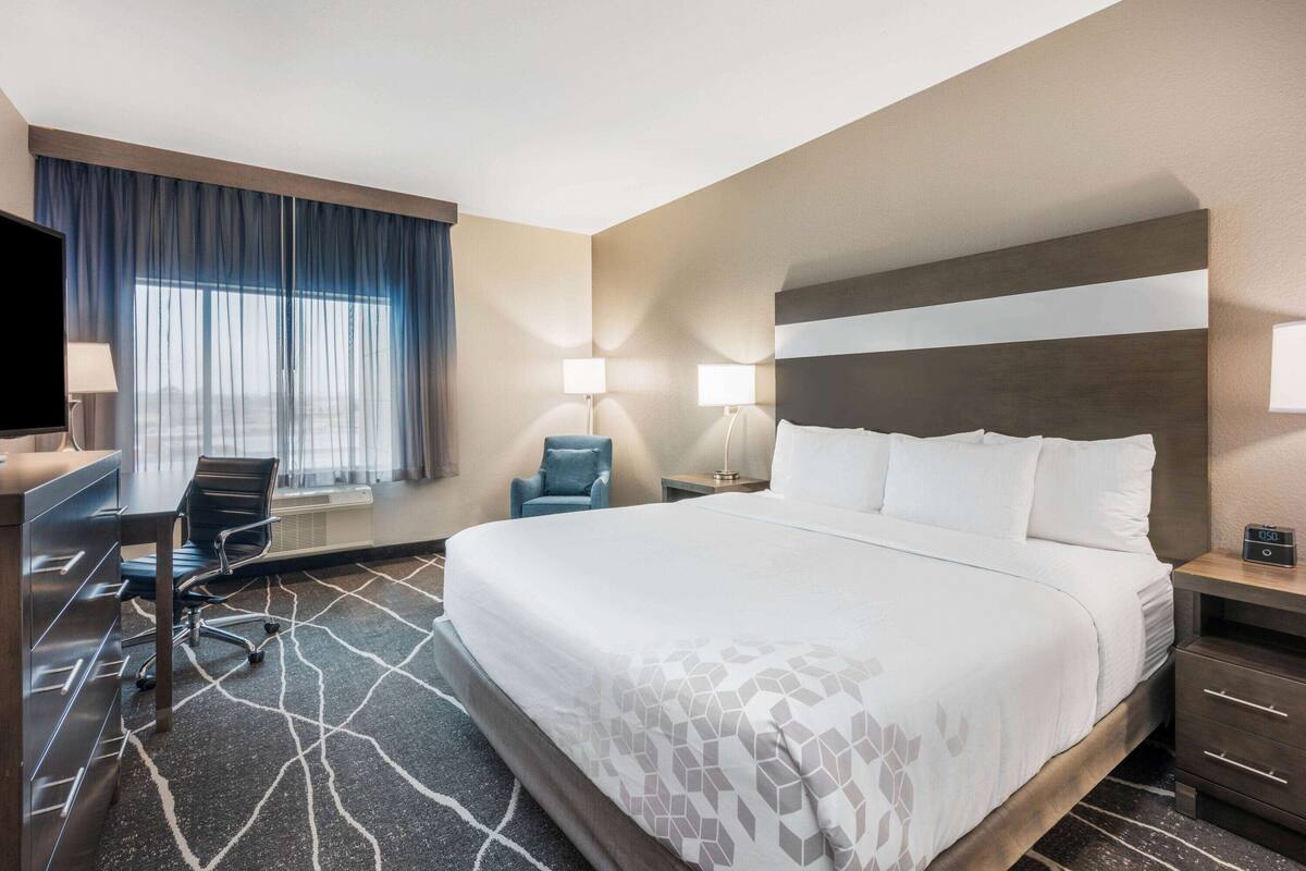 A hotel room with a large bed, a desk with a chair, a TV, and two bedside lamps.