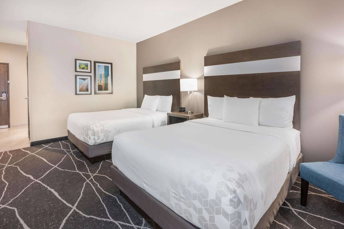 A hotel room with two beds, a desk, a chair, and a wall with framed pictures.