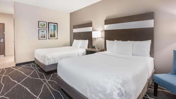A hotel room with two beds, a desk, a chair, and a wall with framed pictures.