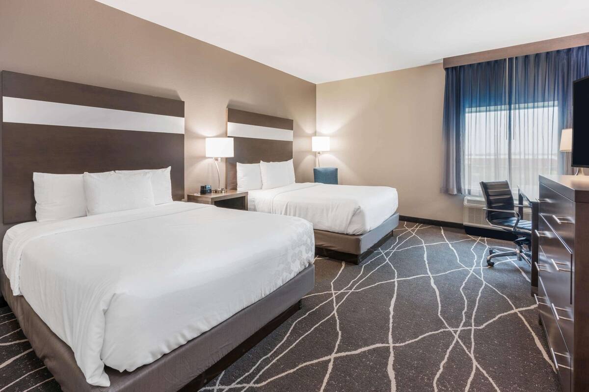A hotel room with two beds, a desk, and a TV.
