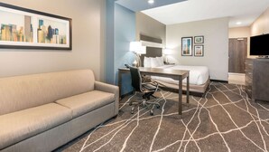 A hotel room with a sofa, desk, chair, bed, and a cityscape painting on the wall. - La Quinta Inn and Suites by Wyndham Houston Spring South (Spring)
