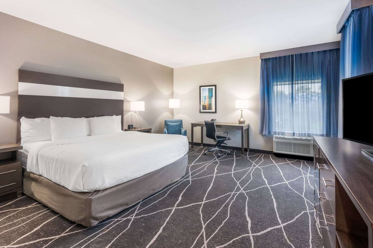 A hotel room with a large bed, a desk with a chair, a television, and a window with curtains.