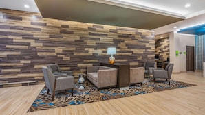A lobby with a modern design, featuring a wooden wall panel, a reception desk, and seating area with a patterned rug. - La Quinta Inn and Suites by Wyndham Houston Spring South (Spring)