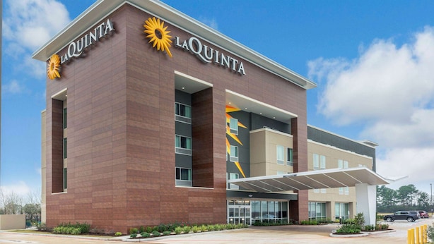 A La Quinta hotel with a modern design, featuring a prominent sun logo and a covered entrance. - La Quinta Inn and Suites by Wyndham Houston Spring South (Spring)