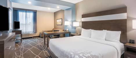 A hotel room with a large bed, a desk, a chair, a TV, and a window with curtains.