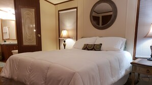 Una cama bien hecha con edredón blanco, una lámpara de noche y un espejo en la pared.