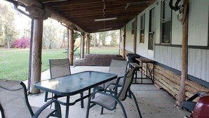 Un área de patio techada con una mesa y sillas, un muro de troncos y vistas al jardín circundante.