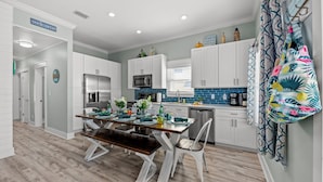 A modern kitchen with white cabinets, a stainless steel refrigerator, a microwave, and a coffee maker. There is a dining table with chairs and a bench. - COZY & CLOSE TO BEACH, VERY CLEAN, PRIVATE POOL, PET FRIEND FEE, LSV DISCOUNT (Destin)