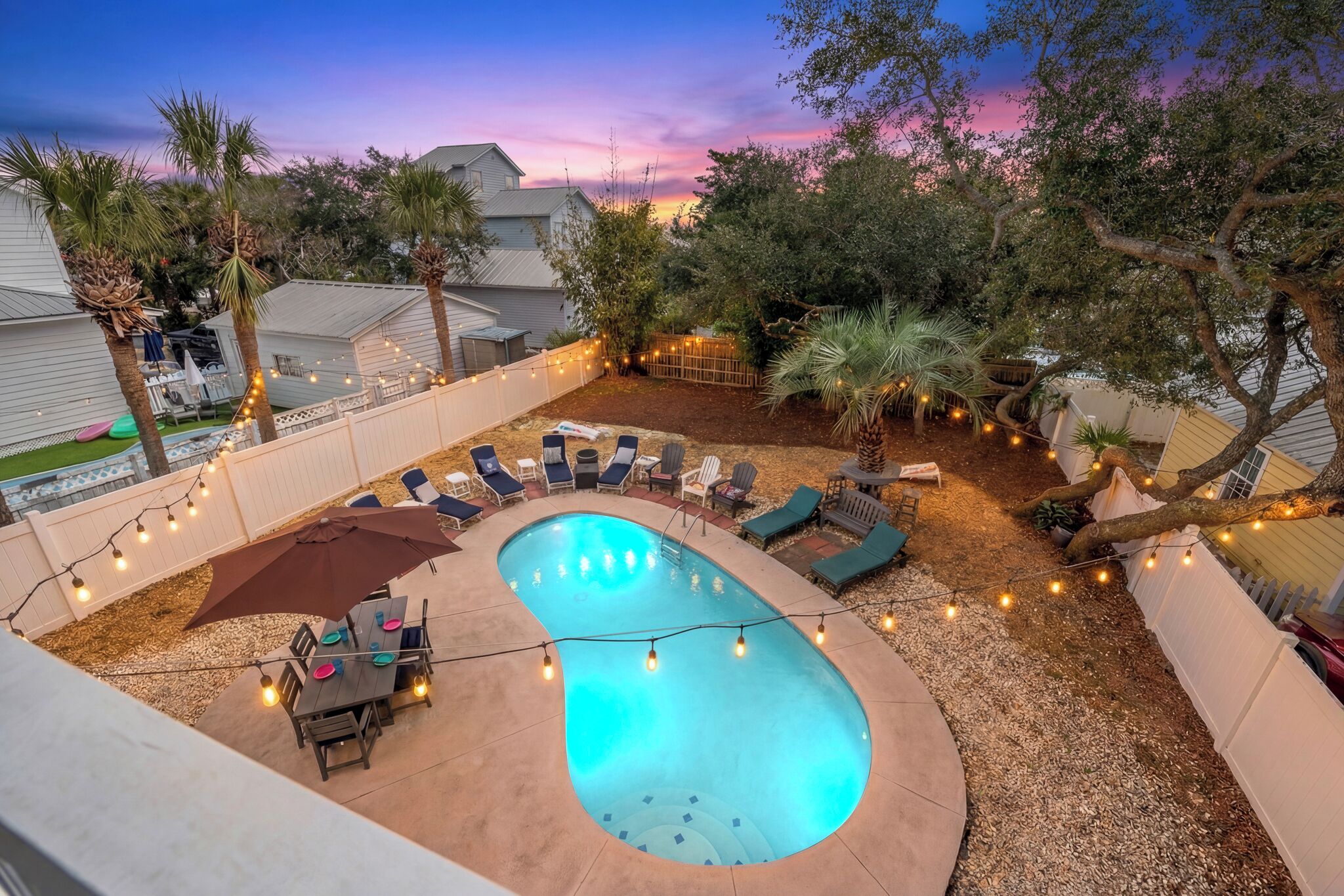 A backyard with a swimming pool, lounge chairs, and string lights.