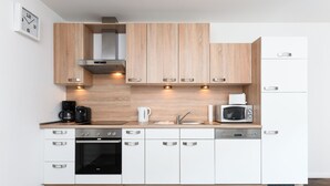 A modern kitchen with wooden cabinets, stainless steel appliances, and a built-in oven. - Vacation apartment Barbara (Wittmund)