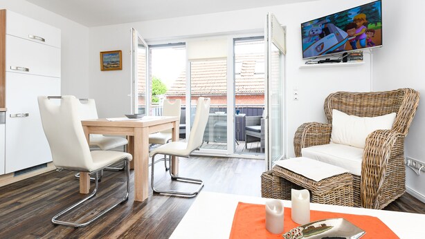 A modern room with a dining table, chairs, a wicker sofa, a TV, and a view of the outside. - Vacation apartment Barbara (Wittmund)