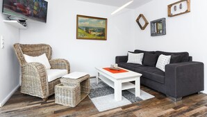 A living room with a television, wicker furniture, a grey sofa, and a painting on the wall. - Vacation apartment Barbara (Wittmund)