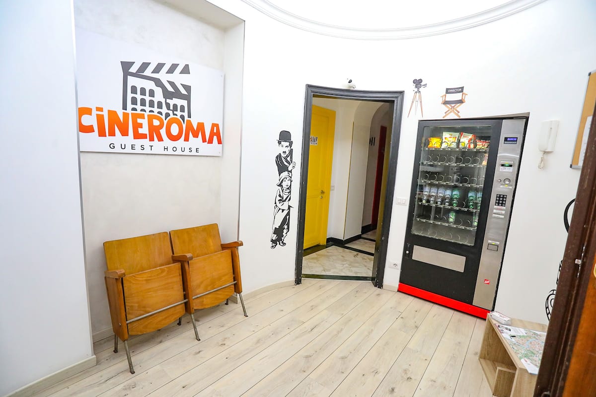 A guest house interior with a cinema-themed sign, a vending machine, and a wooden bench.