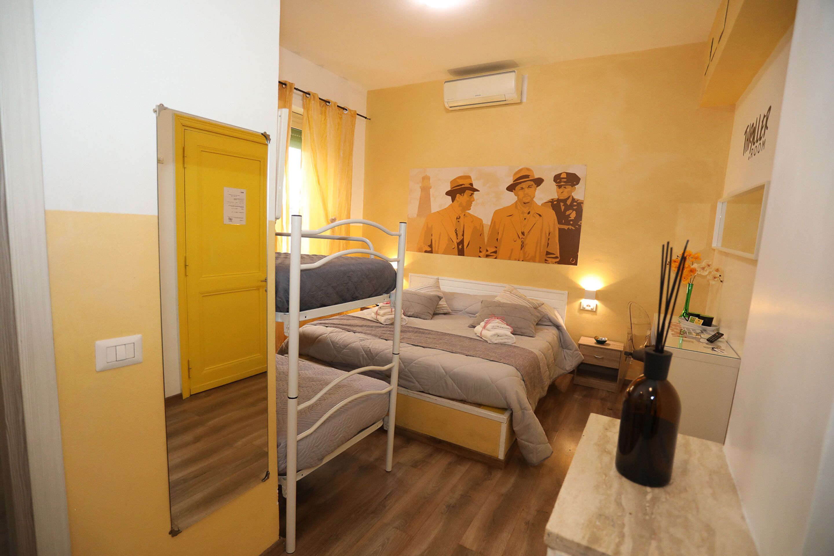 A room with a bunk bed, a bedside table with a vase, a wall-mounted air conditioner, and a poster of police officers.