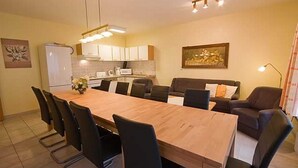 A dining area with a wooden table and black chairs, a kitchen with white cabinets, and a sofa with cushions. - Apartment 3 - House Panorama (Sankt Andreasberg)