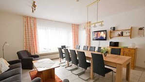 A modern living room with a dining area, a television, and a bookshelf. - Apartment 3 - House Panorama (Sankt Andreasberg)