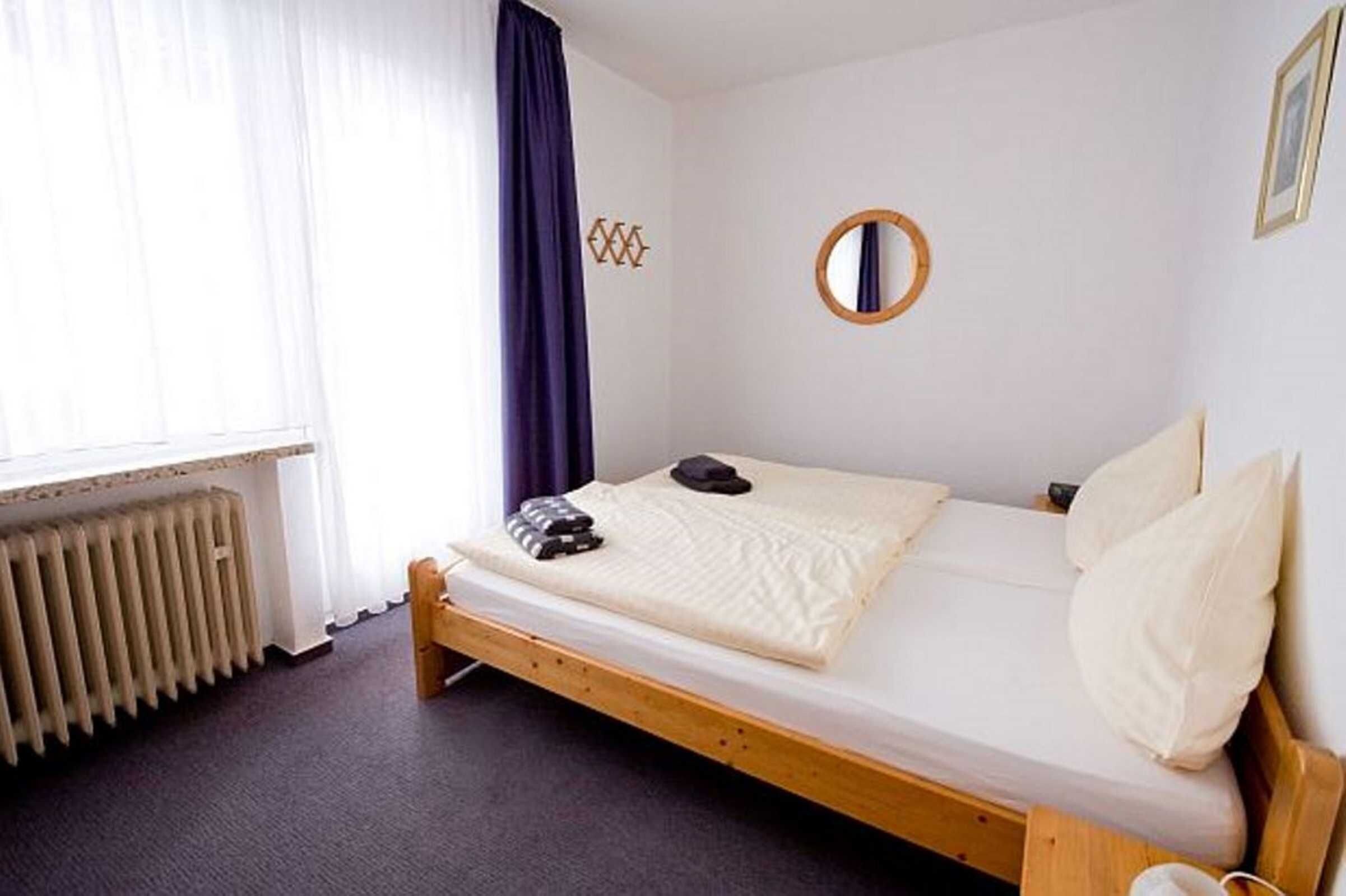 A single bed with a wooden frame, a round mirror on the wall, and a radiator below the window.