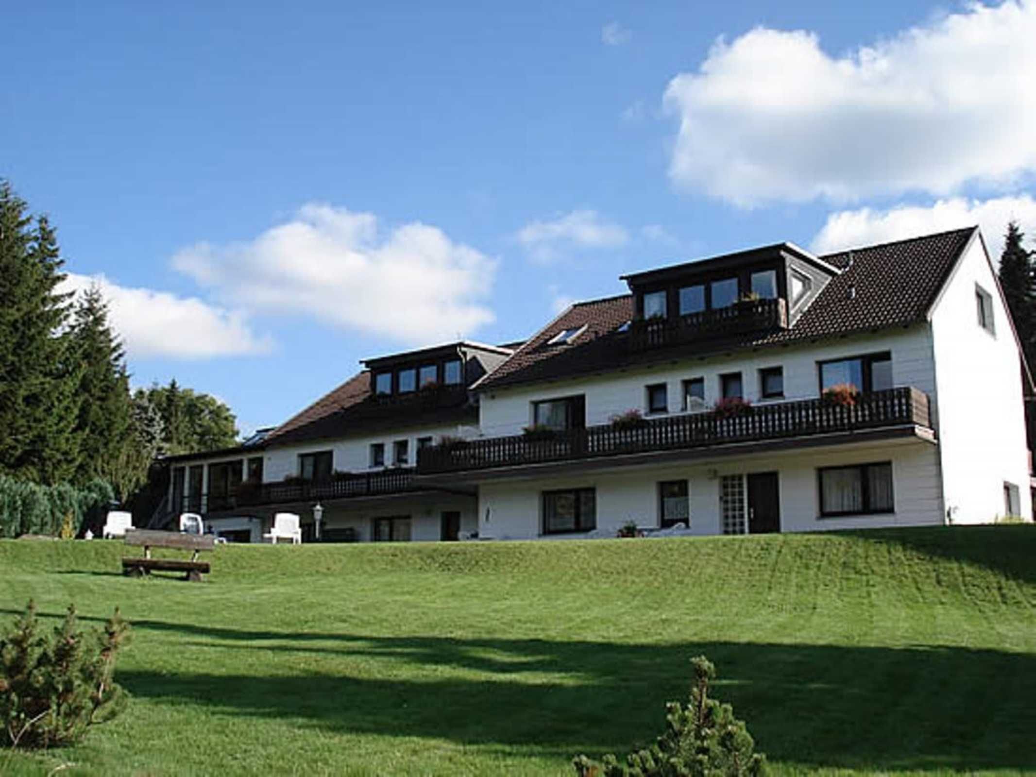 Ein zweistöckiges Gebäude mit geneigtem Dach, mehreren Balkonen und einer Rasenfläche vor der Fassade.
