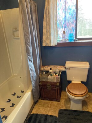 A bathroom with a bathtub, toilet, and a window with curtains. - Quiet, cozy, comfortable, centrally located to the best of the Kenai peninsula. (Soldotna)