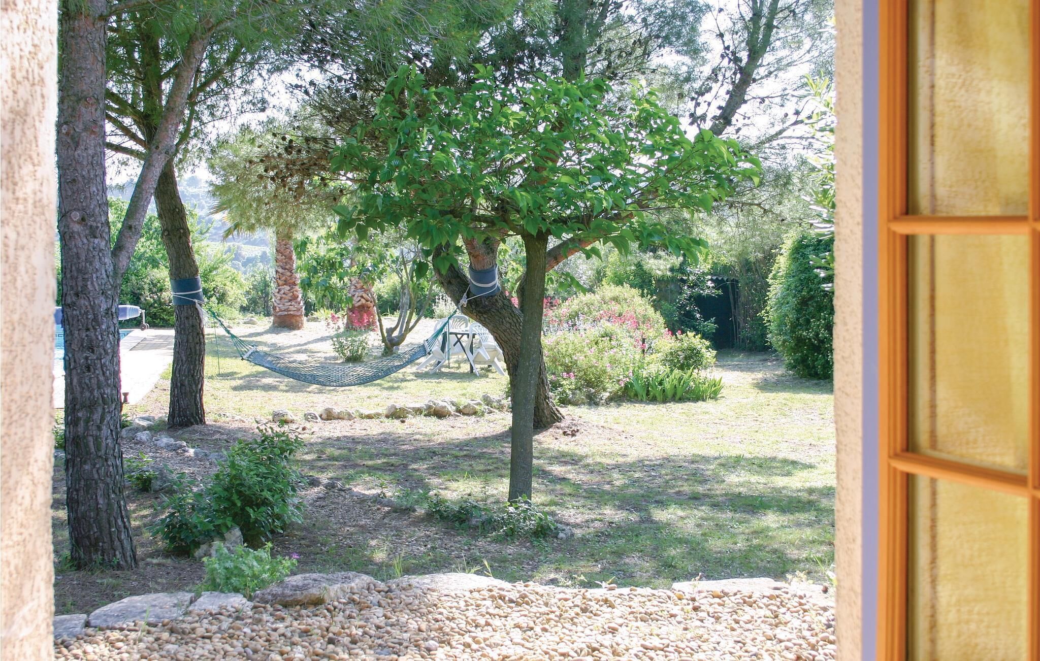 Un jardin avec un hamac, des arbres et une piscine en arrière-plan.
