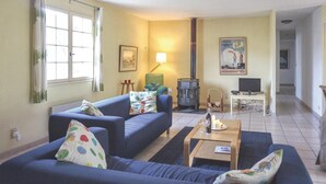 Een woonkamer met twee banken, een tafel, een televisie, een open haard en een raam.